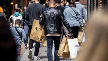 Een man loop in een winkelstraat. Vanaf de achterkant zien we dat hij veel verschillende winkeltassen vast heeft.