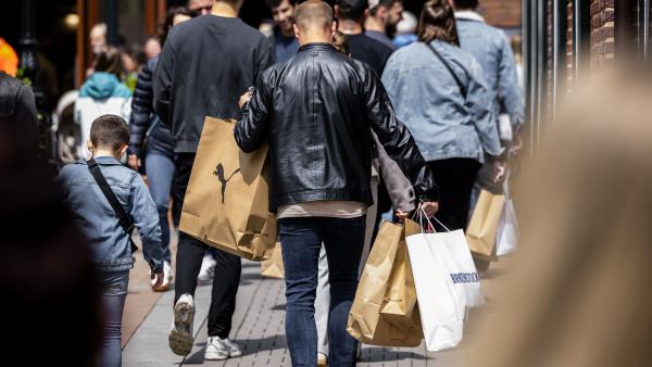 Een man loop in een winkelstraat. Vanaf de achterkant zien we dat hij veel verschillende winkeltassen vast heeft.