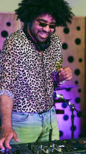 Man met afro en zonnebril en geprinte blouse maakt muziek op dj-set met daarnaast een vrouw die saxofoon speelt