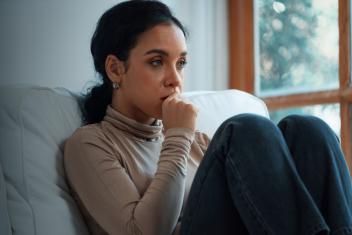 Vrouw staart emotieloos voor zich uit op de bank met hand tegen kind aan