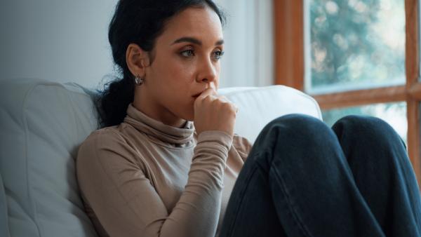 Vrouw staart emotieloos voor zich uit op de bank met hand tegen kind aan