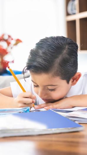 Kind zit over papier heen gebogen en schrijft iets met potlood 