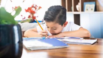 Kind zit over papier heen gebogen en schrijft iets met potlood