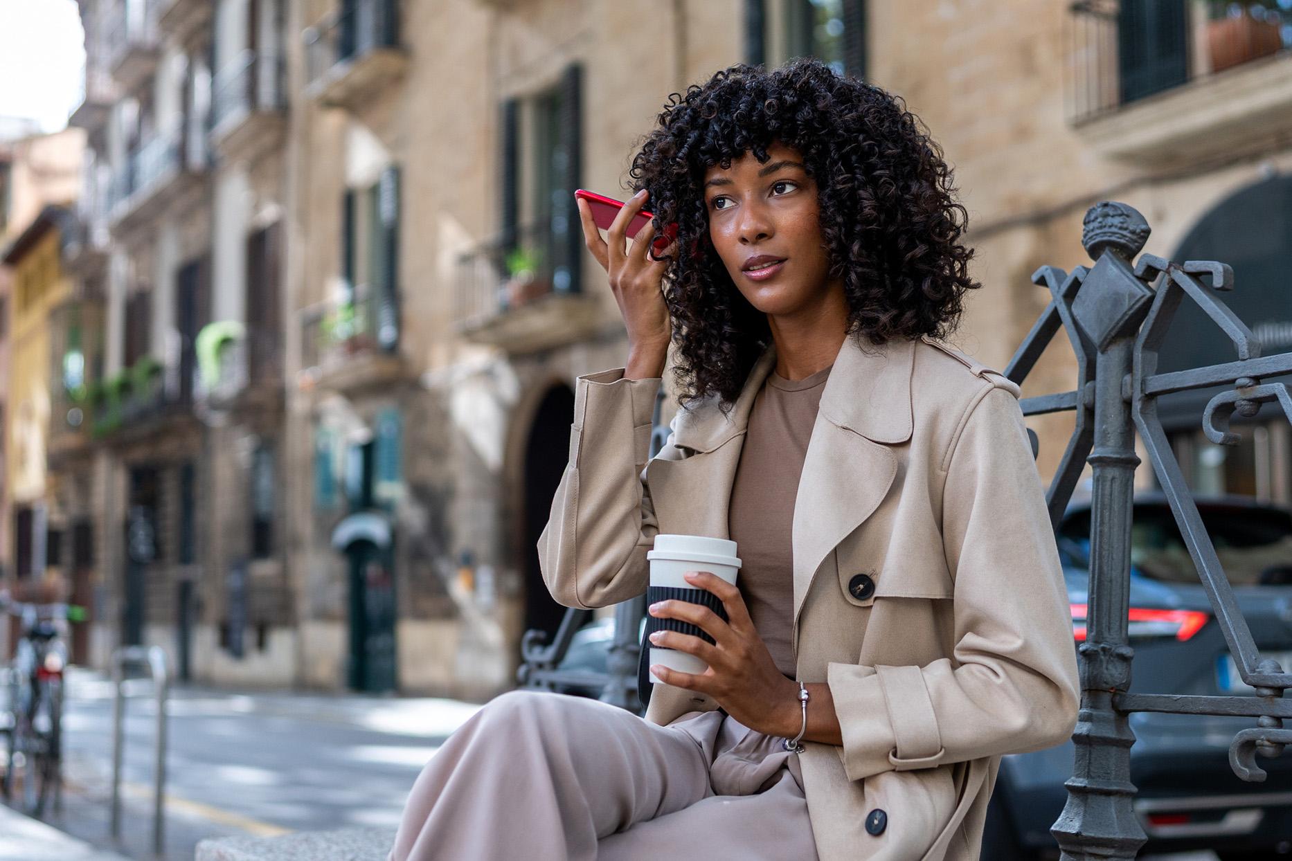 Vrouw belt met telefoon op luidspreker en houdt telefoon bij haar oor zittend op bankje op straat