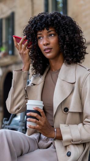Vrouw belt met telefoon op luidspreker en houdt telefoon bij haar oor zittend op bankje op straat