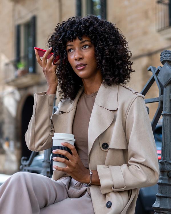 Vrouw belt met telefoon op luidspreker en houdt telefoon bij haar oor zittend op bankje op straat