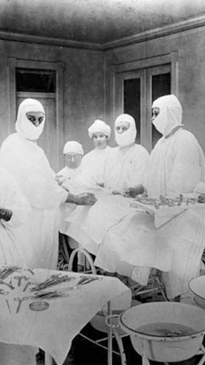 Een zwart wit foto van een operatiekamer waar een deel van de artsen een doek om hun mond gebonden heeft