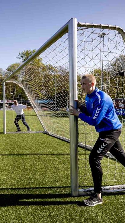 Twee vrijwilligers duwen een goal over het voetbalveld.