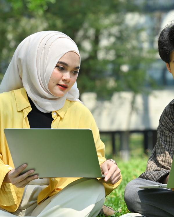 Een jongen en een meisje zitten samen buiten met hun laptops