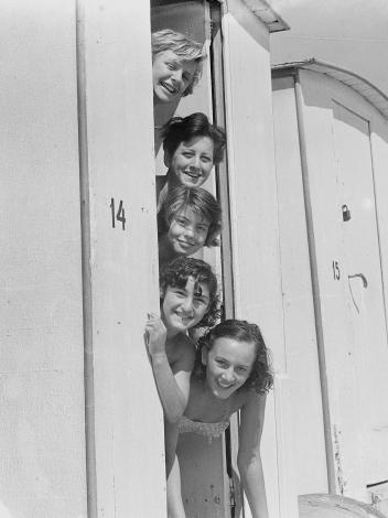 Een zwart-witfoto van vijf vrouwen verticaal op een rij met hun hoofden uit een strandwagentje 