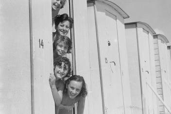 Een zwart-witfoto van vijf vrouwen verticaal op een rij met hun hoofden uit een strandwagentje 
