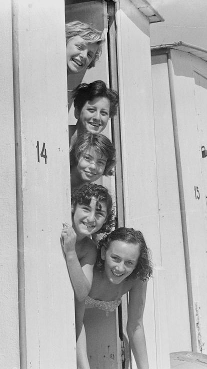 Een zwart-witfoto van vijf vrouwen verticaal op een rij met hun hoofden uit een strandwagentje 