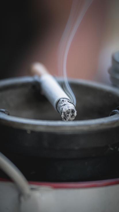 Brandende sigaret ligt op de rand van een asbak 