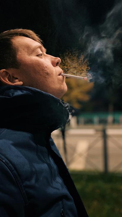 Zijaanzicht van jongen in winterjas met brandende sigaret in zijn mond en rook om hem heen