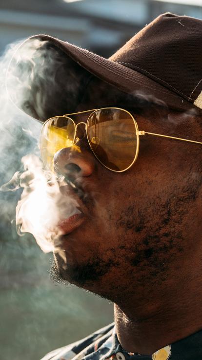 Man met zonnebril en pet blaast sigarettenrook uit