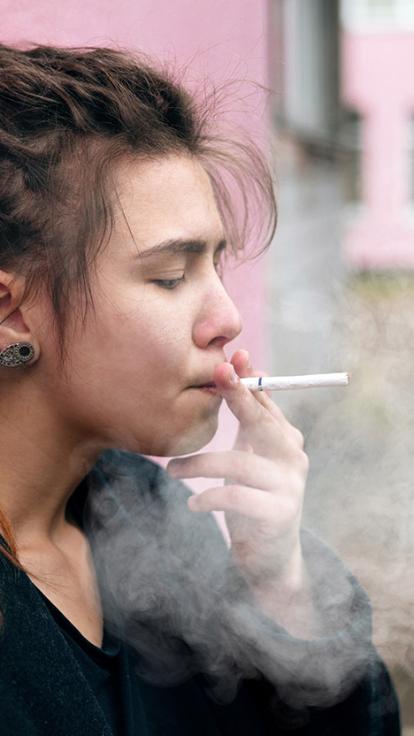 Meisje met dreadlocks leunt tegen muur en rookt een sigaret