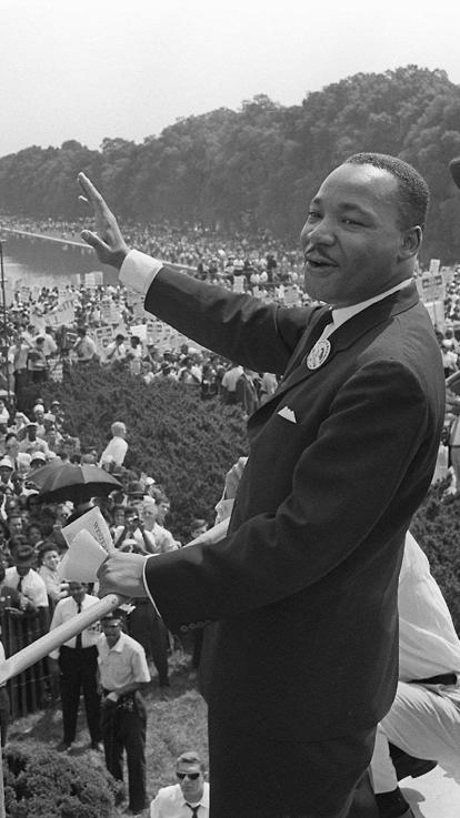 Martin Luther King jr. zwaait naar een grote mensenmassa die naar zijn speech luistert in Washington D.C. op een zwart-witfoto