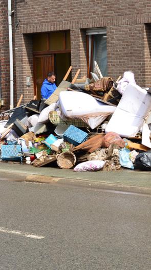 Man staat bij een berg grofvuil en meubels op straat te kijken. 