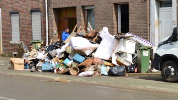 Man staat bij een berg grofvuil en meubels op straat te kijken. 