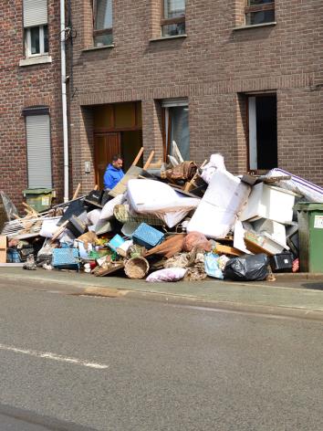 Man staat bij een berg grofvuil en meubels op straat te kijken. 