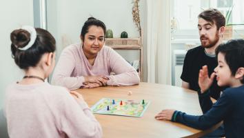 twee volwassenen en twee kinderen spelen samen een bordspelletje aan tafel