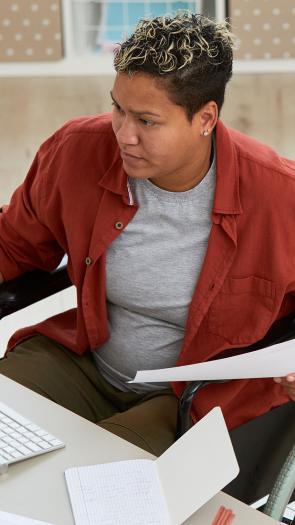 Iemand in een rolstoel achter haar bureau aan het werk, kijkend naar het computerscherm