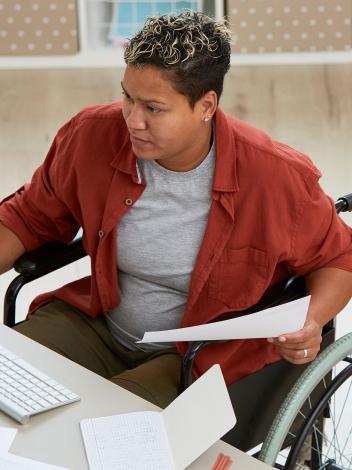 Iemand in een rolstoel achter haar bureau aan het werk, kijkend naar het computerscherm