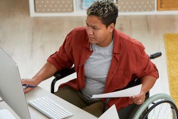Iemand in een rolstoel achter haar bureau aan het werk, kijkend naar het computerscherm