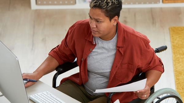 Iemand in een rolstoel achter haar bureau aan het werk, kijkend naar het computerscherm