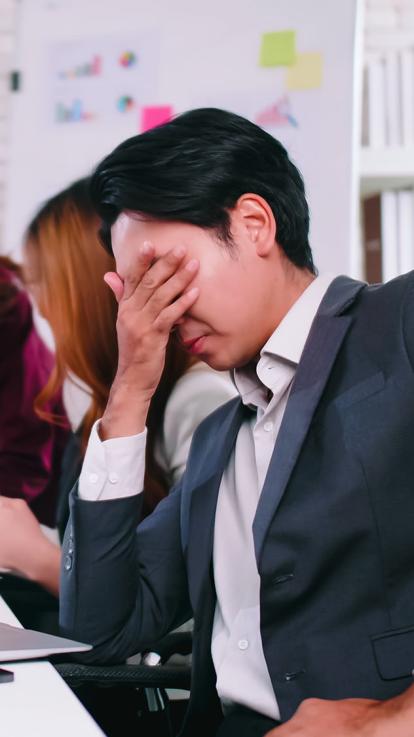 Een man in pak met zijn hand voor zijn gezicht achter zijn laptop, zichtbaar aangeslagen