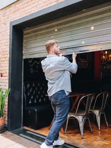 een man doet de roldeur van zijn horecazaak dicht