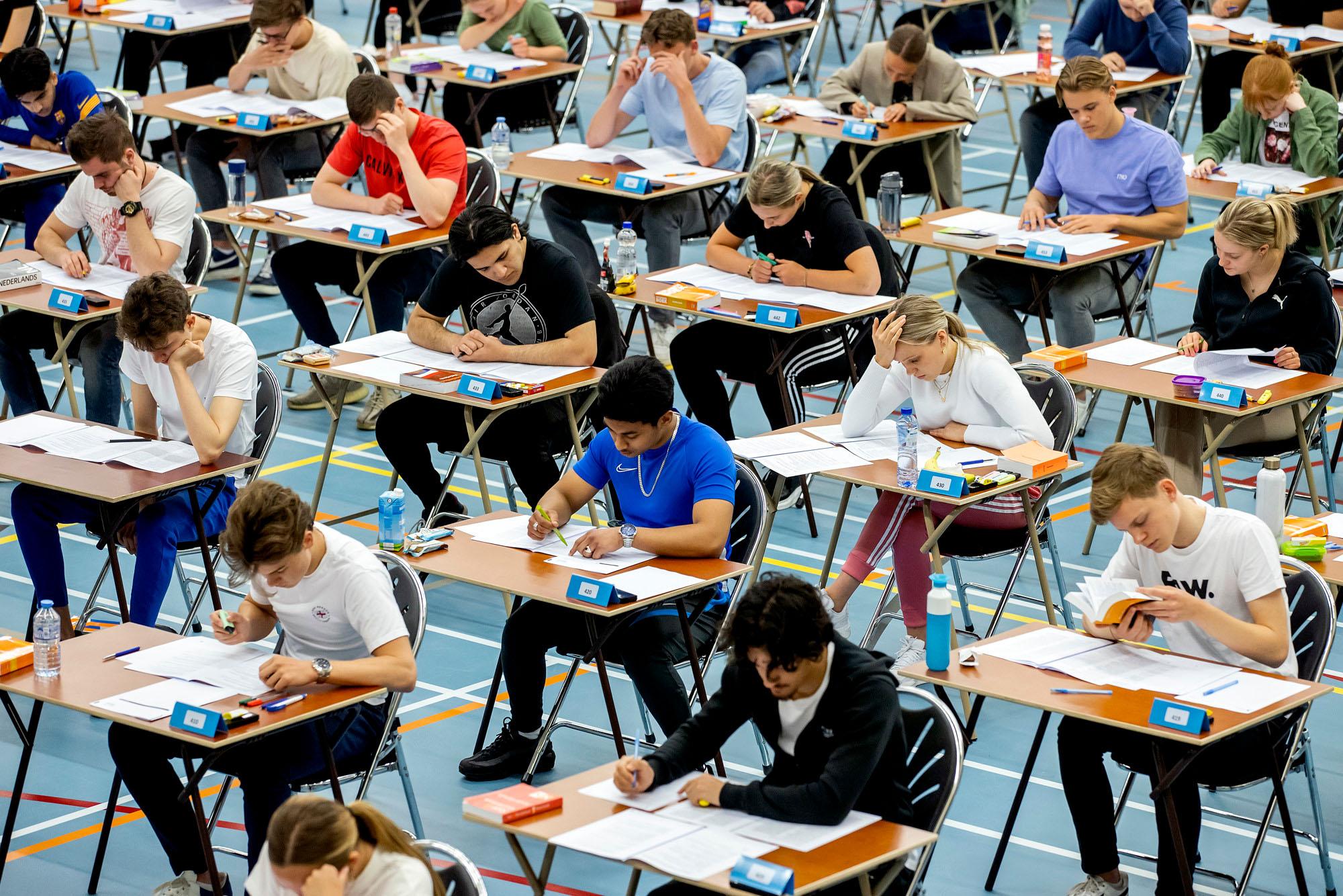 Scholieren maken hun eindexamens aan tafeltjes in een gymzaal