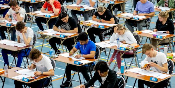 Scholieren maken hun eindexamens aan tafeltjes in een gymzaal