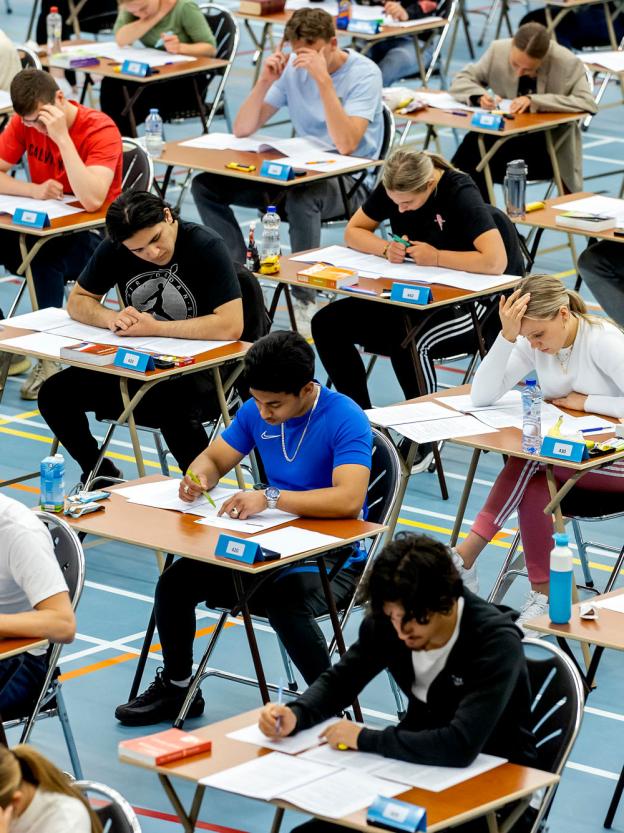 Scholieren maken hun eindexamens aan tafeltjes in een gymzaal