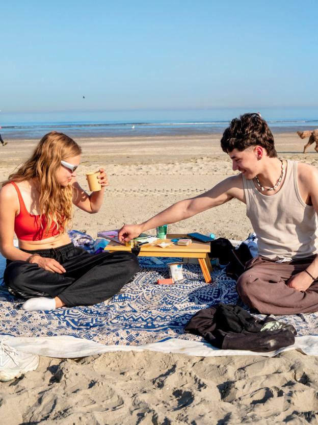 Twee jongeren op kleedjes op het strand, op een zonnige dag met de zee op de achtergrond