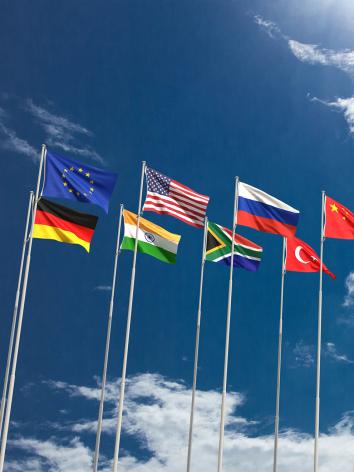 vlaggenmasten met vlaggen van verschillende landen en organisaties, met een blauwe lucht op de achtergrond