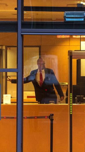 Foto door raam van rechtbank heen waar een bode achter de balie naar een deur wijst