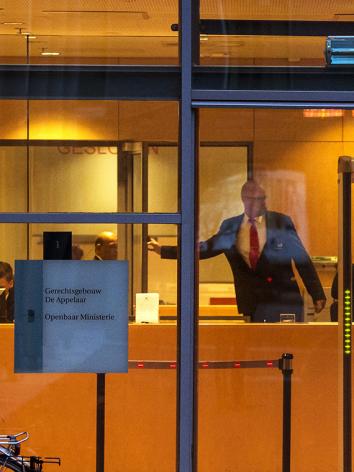 Foto door raam van rechtbank heen waar een bode achter de balie naar een deur wijst