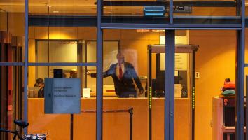 Foto door raam van rechtbank heen waar een bode achter de balie naar een deur wijst