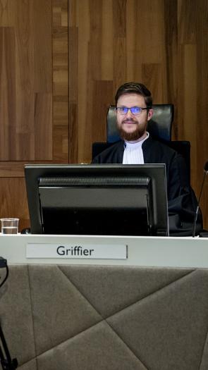 Rechter en griffier zitten in de rechtbank achter tafel. Griffier zit achter computerscherm