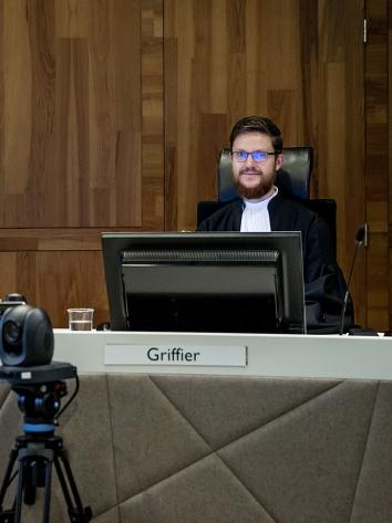 Rechter en griffier zitten in de rechtbank achter tafel. Griffier zit achter computerscherm