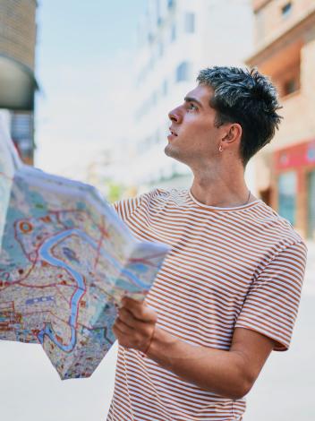 Een man staat alleen op straat en kijkt verward omhoog, met een kaart van de stad in zijn handen