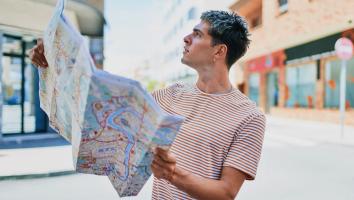 Een man staat alleen op straat en kijkt verward omhoog, met een kaart van de stad in zijn handen