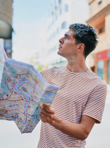 Een man staat alleen op straat en kijkt verward omhoog, met een kaart van de stad in zijn handen