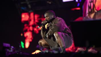 Kanye West hurkend op podium met microfoon bij zijn mond