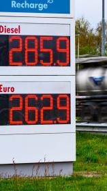 Brandstofprijzen op een bord van een tankstation (2,85 voor Diesel en 2.62 voor Benzine) met een langsrijdende vrachtwagen