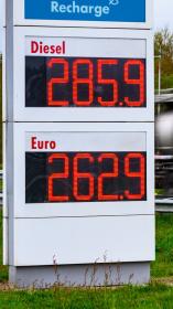 Brandstofprijzen op een bord van een tankstation (2,85 voor Diesel en 2.62 voor Benzine) met een langsrijdende vrachtwagen