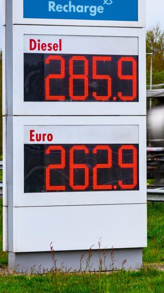 Brandstofprijzen op een bord van een tankstation (2,85 voor Diesel en 2.62 voor Benzine) met een langsrijdende vrachtwagen