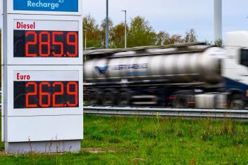 Brandstofprijzen op een bord van een tankstation (2,85 voor Diesel en 2.62 voor Benzine) met een langsrijdende vrachtwagen