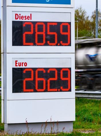 Brandstofprijzen op een bord van een tankstation (2,85 voor Diesel en 2.62 voor Benzine) met een langsrijdende vrachtwagen